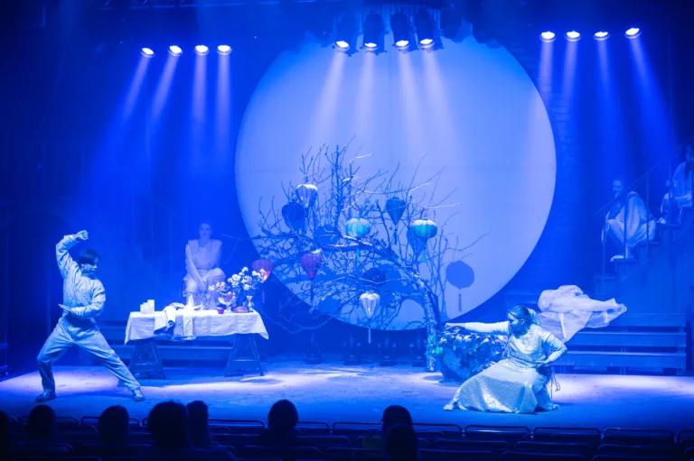 En bild ur pjäsen Månskensprinsen där två skådespelare dansar i blått sken. Kuva Månskensprinsen näytelmästä jossa kaksi näyttelijää tanssivat sinertävässä valaistuksessa.